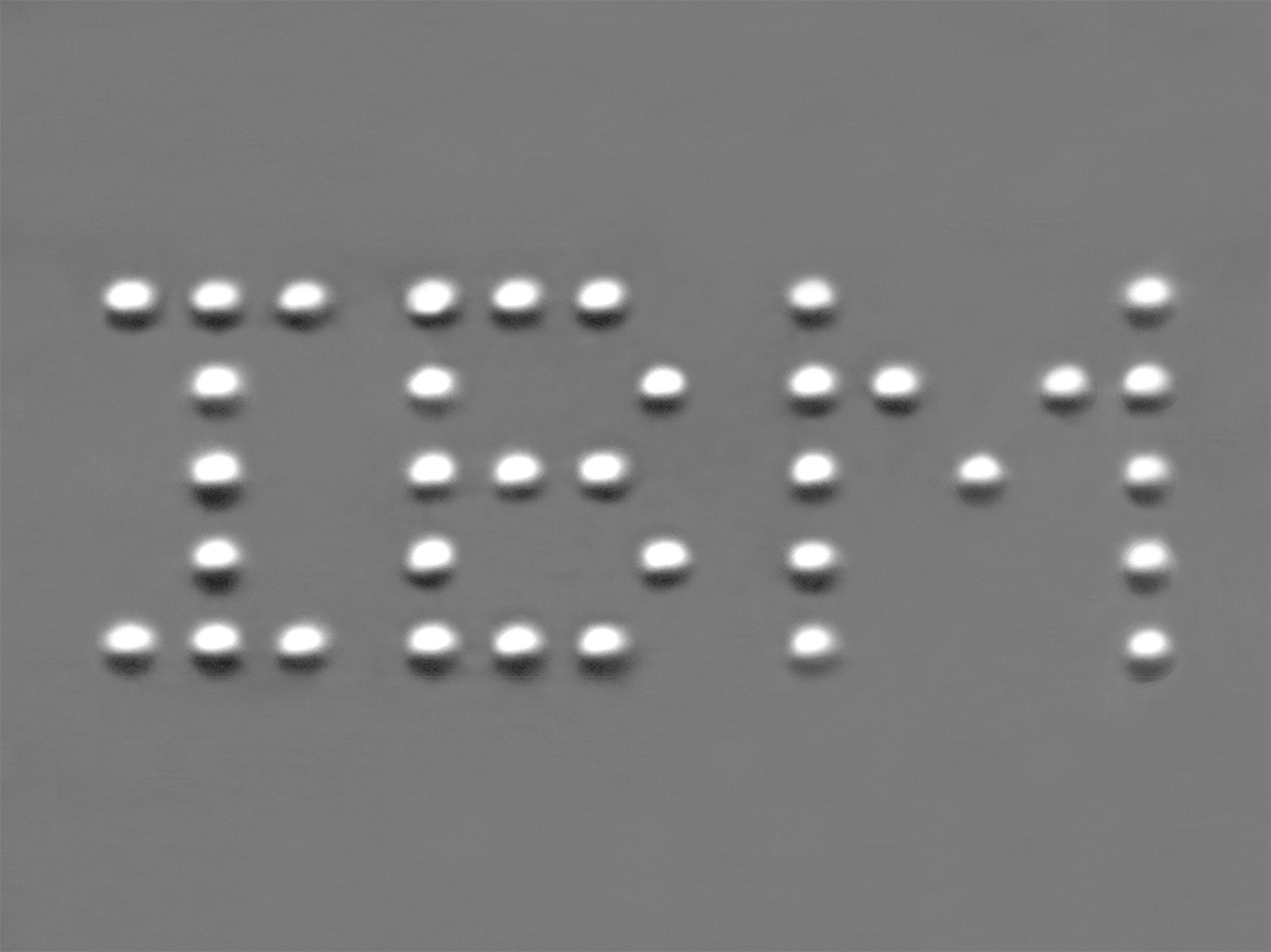 A field of dark gray, dotted by 35 spherules, representing atoms of xenon, all of which spell out the acronym IBM in capital letters: 9 dots for I; 13 dots for B; and 13 dots for M.
